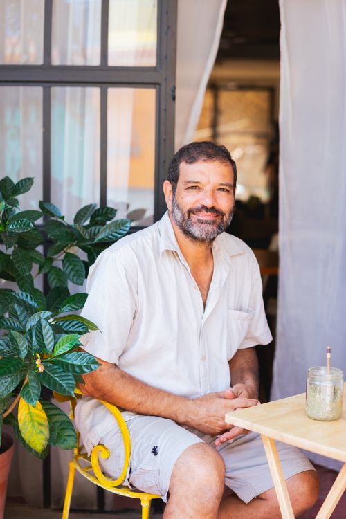 Free A cheerful man with a beard sits outdoors next to a lush plant, enjoying a sunny day. Stock Photo