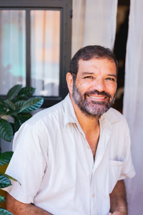 Free Smiling man with a beard sitting outside wearing a button-up shirt, creating a warm and welcoming vibe. Stock Photo