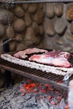 Two juicy steaks with sausages grilling over hot coals on a stone barbecue.