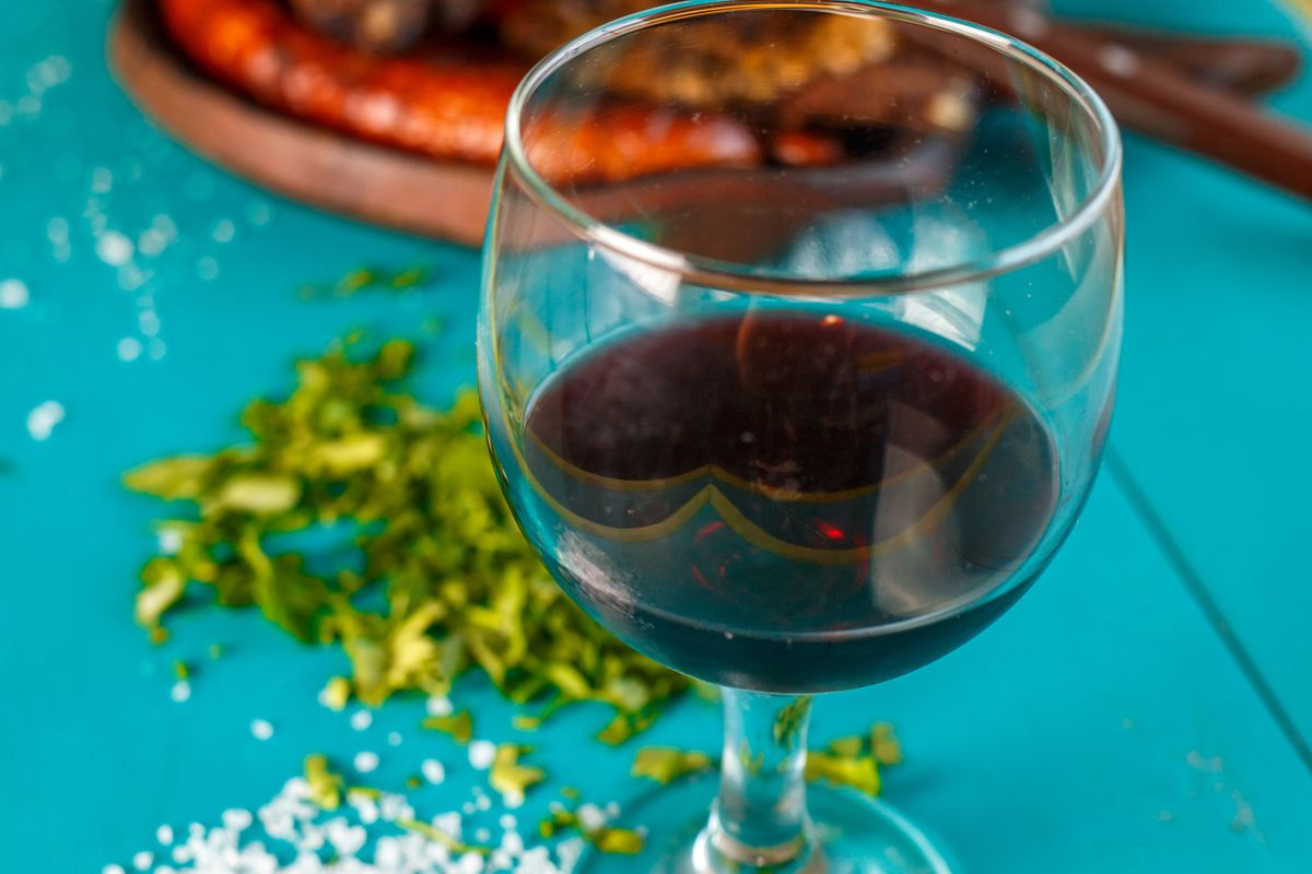 Copa de vino tinto junto a un asado argentino