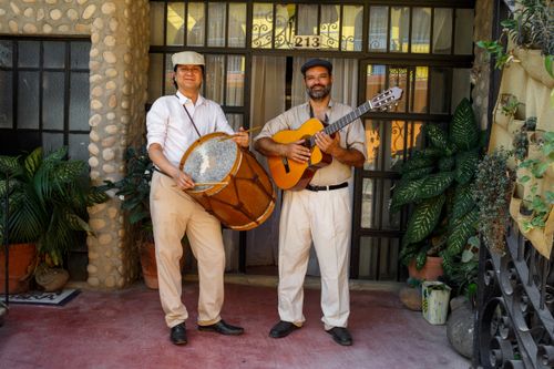 Free Two Hispanic musicians playing a guitar and a drum, posing outdoors in a traditional setting. Stock Photo