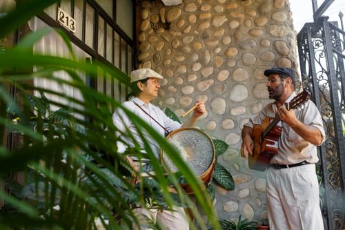 Free Musicians playing guitar and drum outside a rustic stone house, capturing cultural heritage. Stock Photo