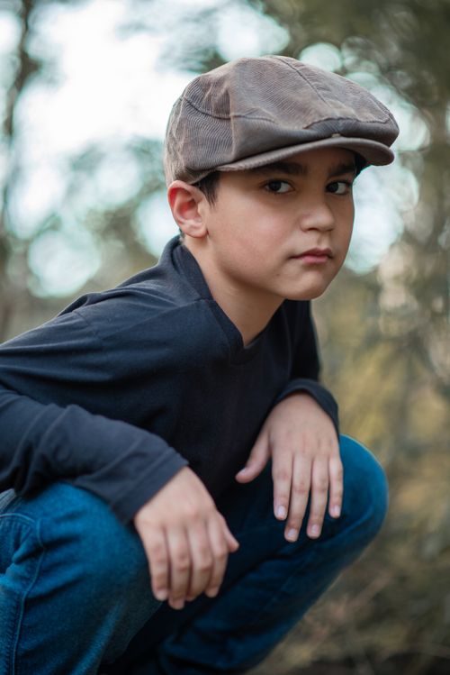 Free A young boy posing outdoors in stylish attire with a hat and blue long sleeves, exuding confidence. Stock Photo