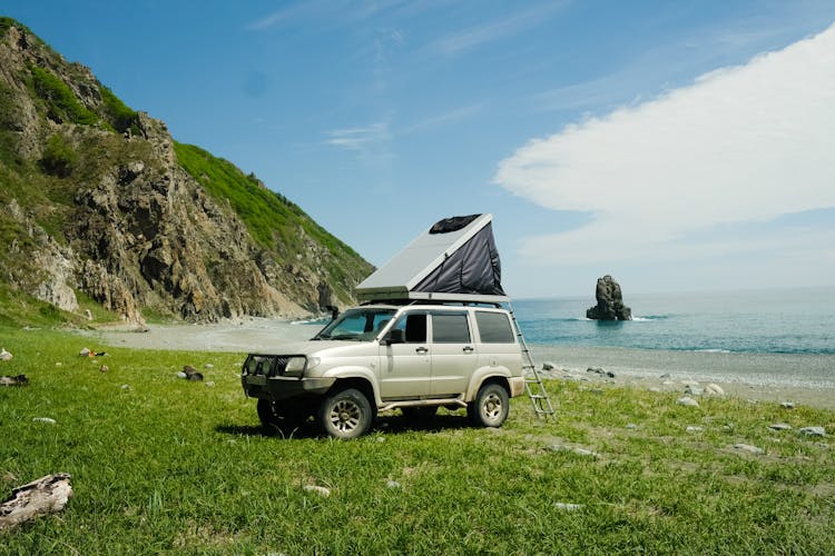 White SUV Parked On A Grass Field Near The Beach