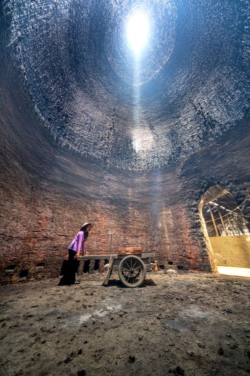 Free Asian woman working in a traditional brick kiln with sunlight highlighting the structure. Stock Photo
