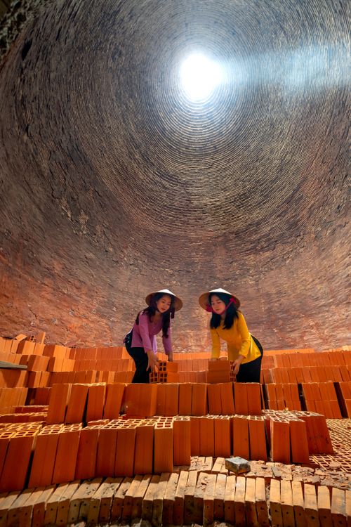 Free Two women stacking bricks inside a kiln, wearing traditional hats. Stock Photo