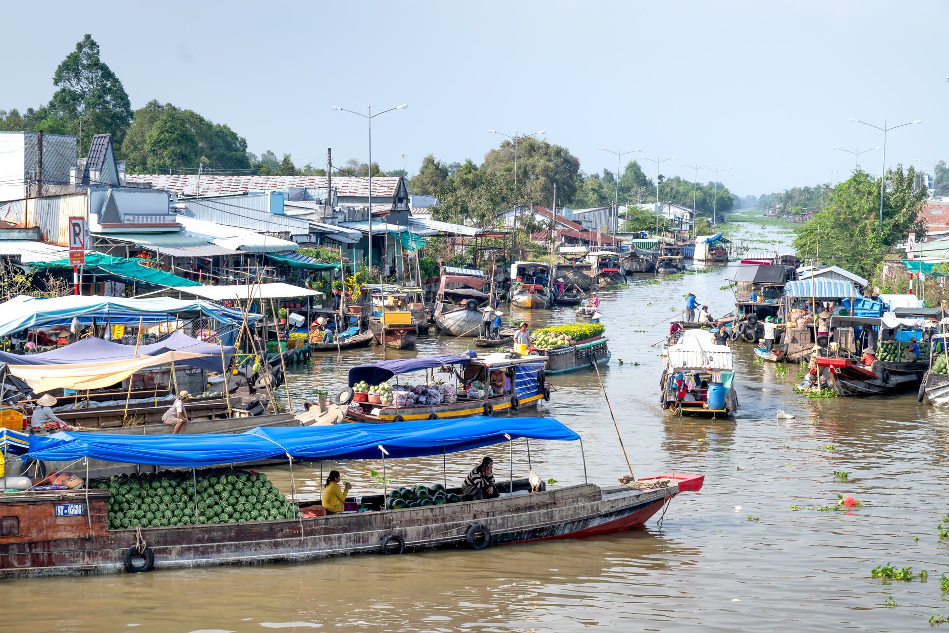 A bustling floating market with boats selling goods on a lively canal in a rural setting.