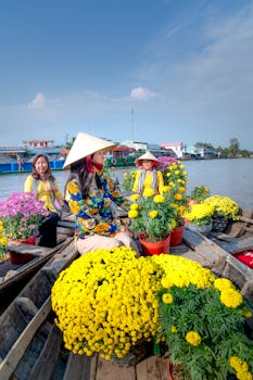 Women in traditional attire selling vibrant flowers on a floating market boat under a sunny sky.