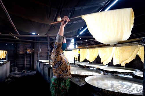 Free Asian woman making rice paper in a traditional Vietnamese setting indoors. Stock Photo