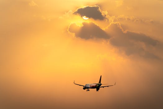 A commercial airplane flying beneath a dramatic golden sunset sky with clouds.