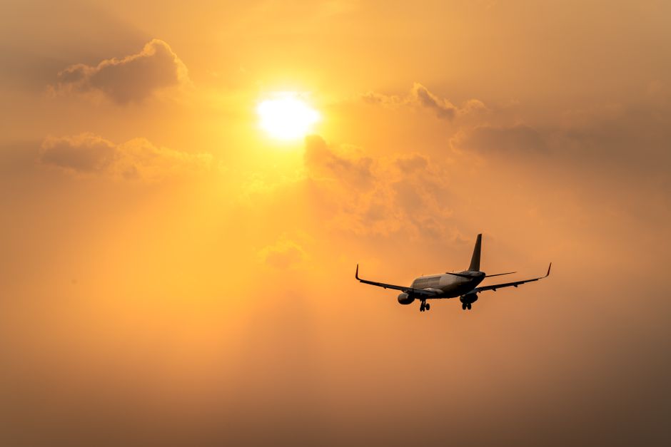 Silhouette of an airplane flying towards a vibrant sunset sky with warm orange hues.