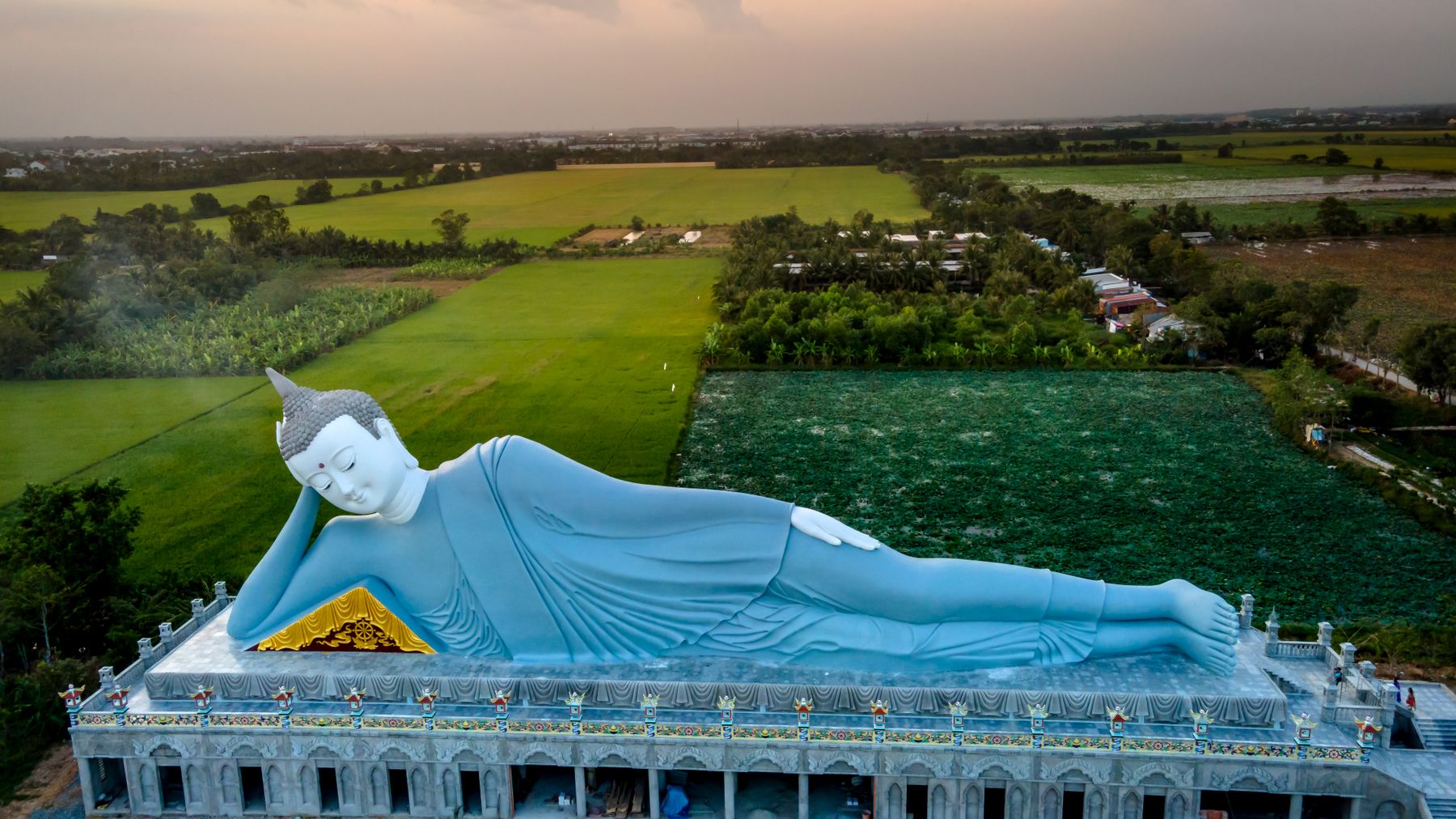 A breathtaking aerial image of the reclining Buddha statue surrounded by lush green fields at sunset.