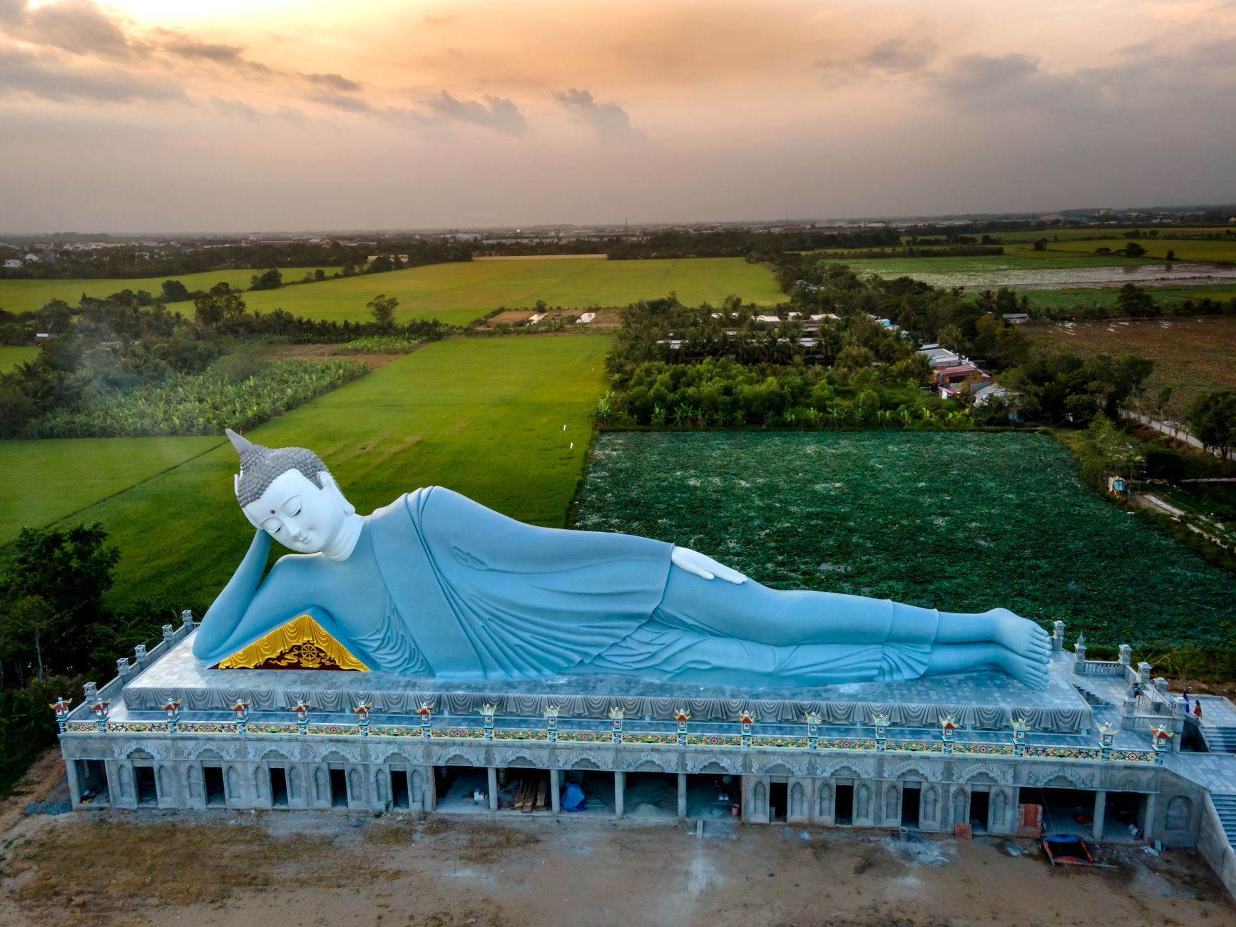 A breathtaking aerial image of the reclining Buddha statue surrounded by lush green fields at sunset.