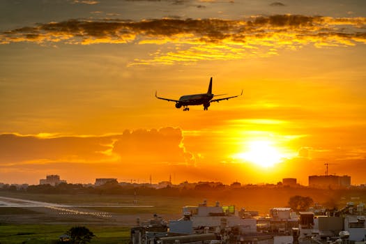 A commercial airplane lands during a vibrant sunset, creating a dramatic sky backdrop.