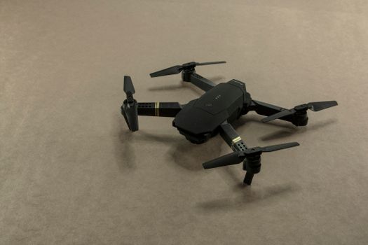 A compact black drone rests on a plain brown carpet. Ideal for technology and aviation themes.