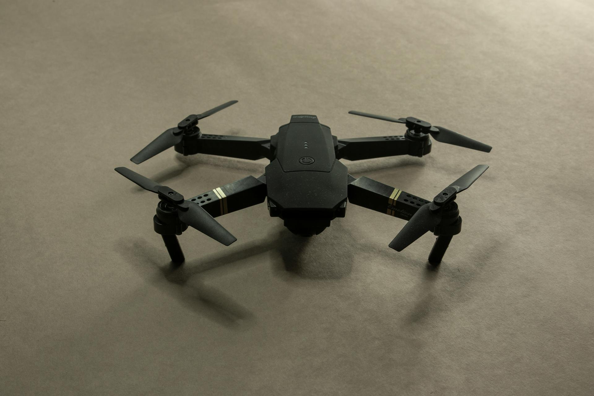 Close-up shot of a small black drone with propellers on a neutral backdrop.