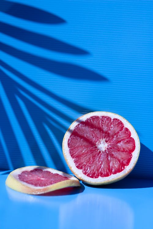 Free Vibrant sliced grapefruit on a blue surface with dramatic shadows of palm leaves. Stock Photo
