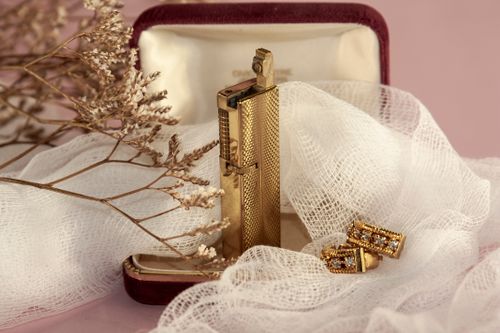 Free Close-up of a luxury gold lighter and earrings placed on elegant white fabric with decorative dried flowers. Stock Photo