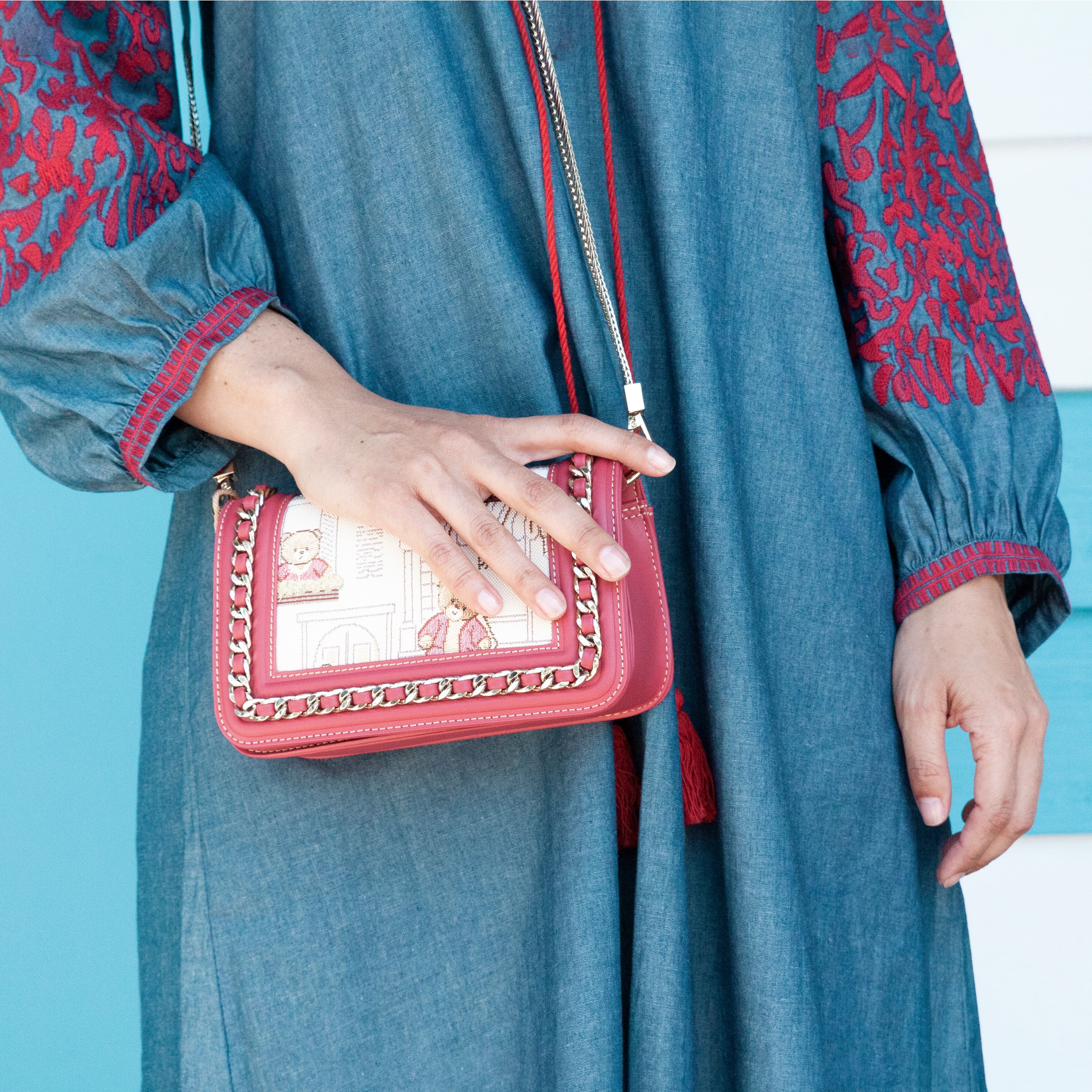 Close-up of a woman's hand holding an embroidered purse against a blue background.