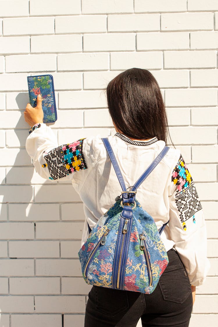 A Person In White Long Sleeve Shirt Facing A Brick Wall Holding A Blue Wallet 