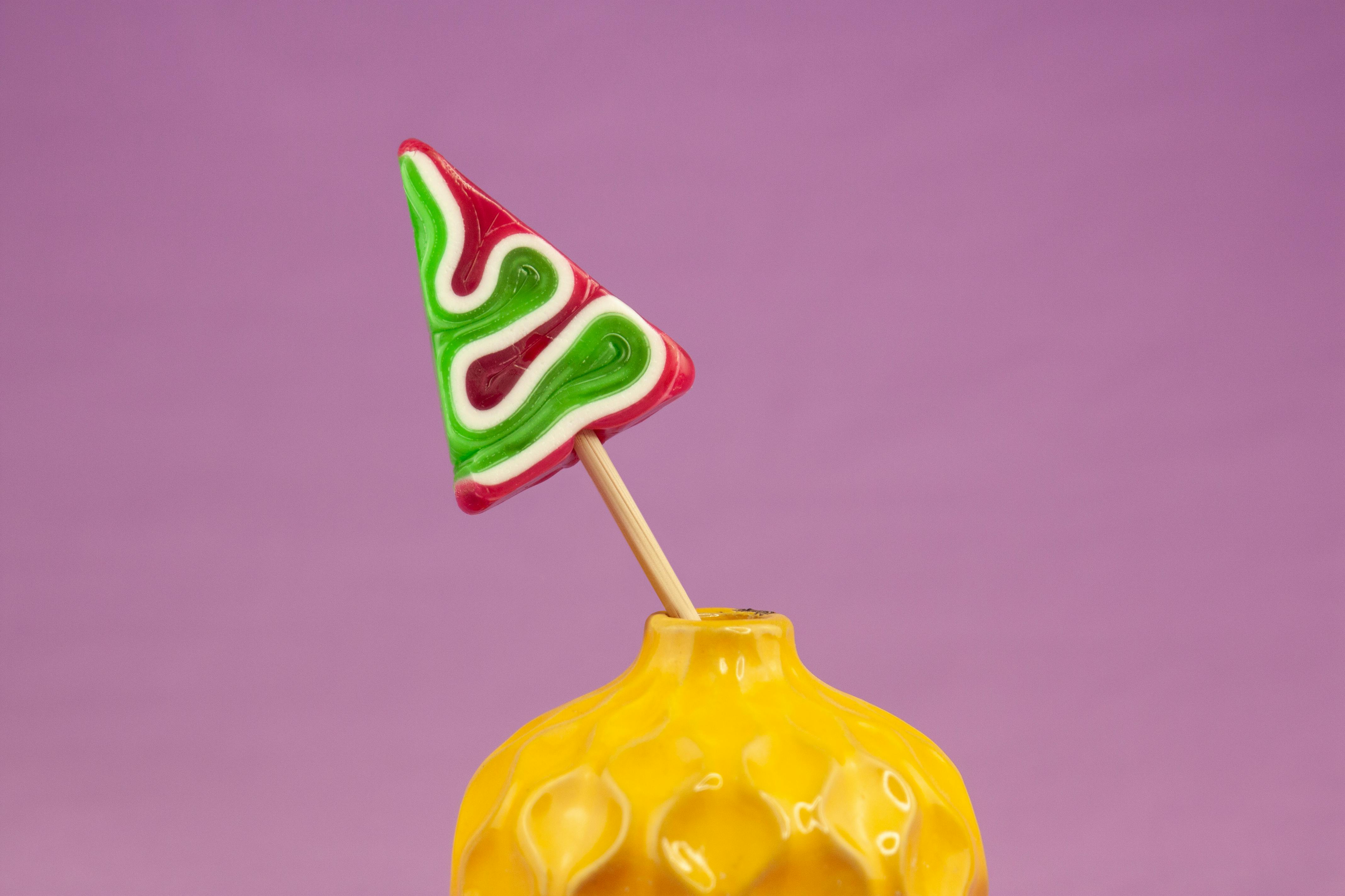 Close-up of a vibrant spiral lollipop in a yellow vase against a pink background, highlighting sweetness and fun.