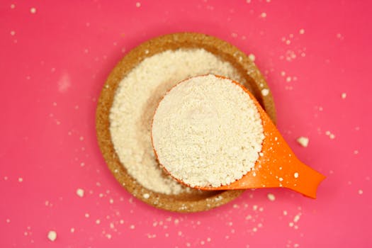 An orange measuring spoon filled with flour on a vibrant pink background. Perfect for baking themes.