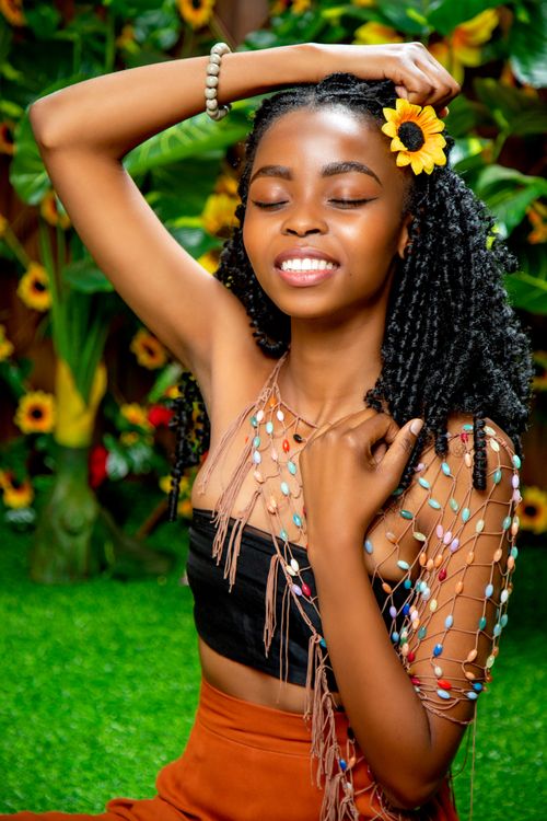 Free Smiling woman with sunflower in black hair, eyes closed, in a vibrant green garden setting. Stock Photo