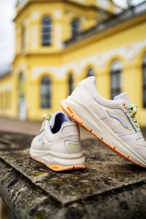 Free Stylish white sneakers displayed on a concrete surface with a yellow building backdrop. Stock Photo
