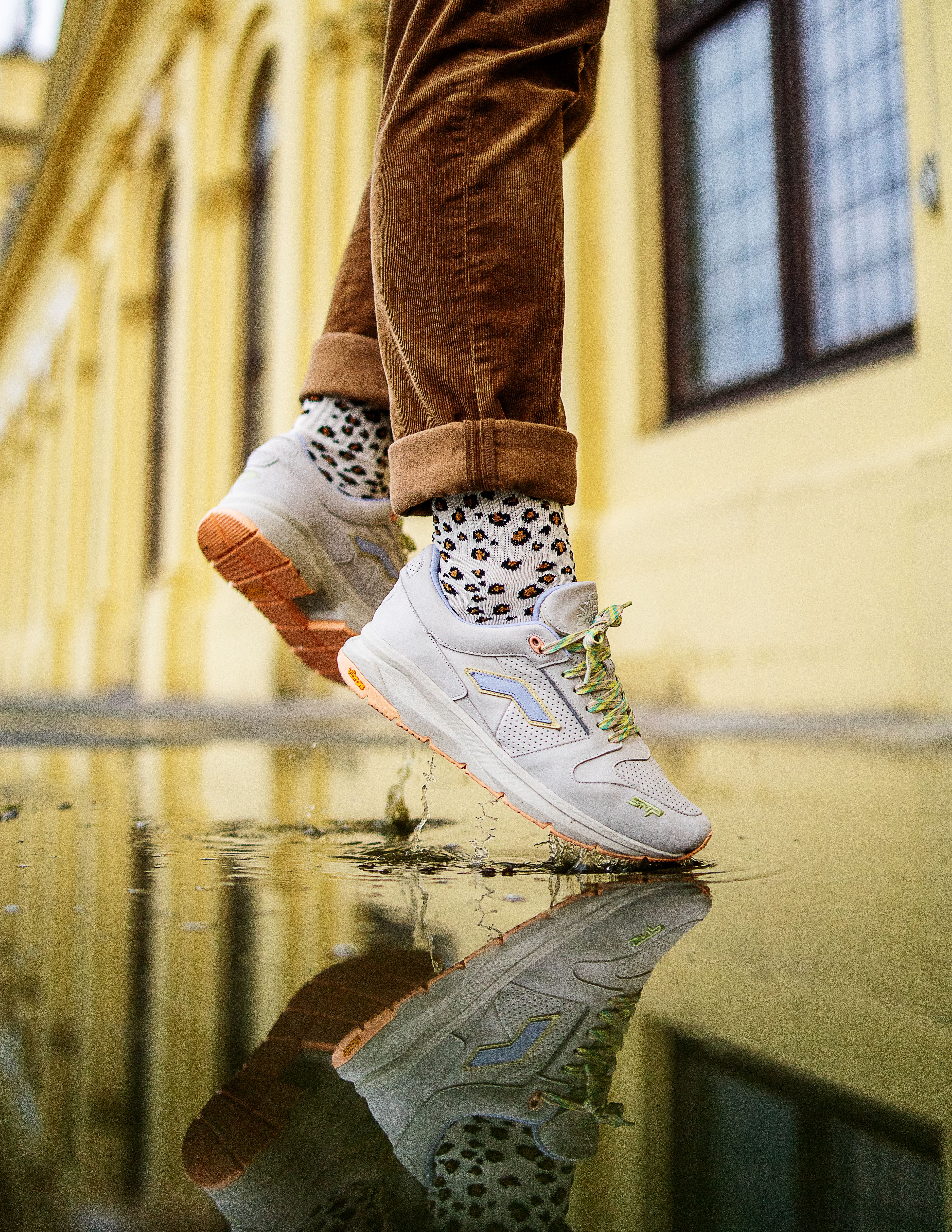 Stylish leap over puddle with vibrant reflection, showcasing trendy sneakers.