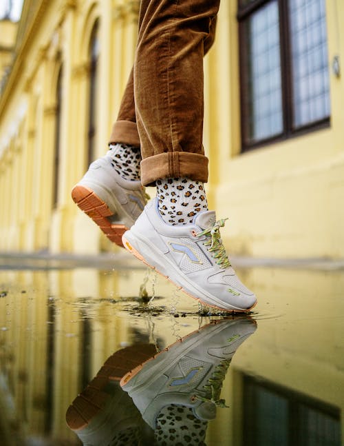 A Person in White Sneakers Wearing Brown Pants while Jumping on Wet Ground