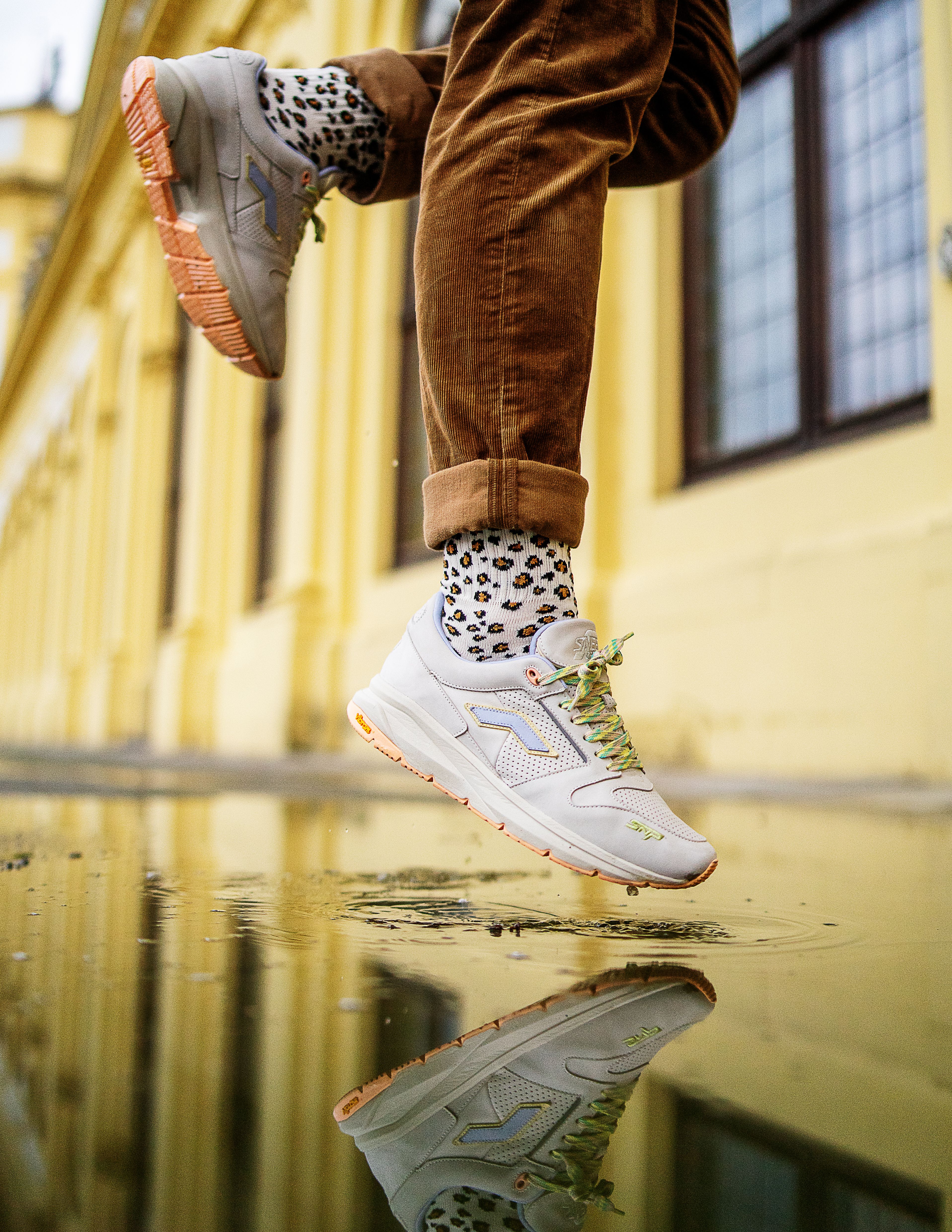 A person jumps over a reflective puddle showcasing stylish sneakers and leopard print socks.