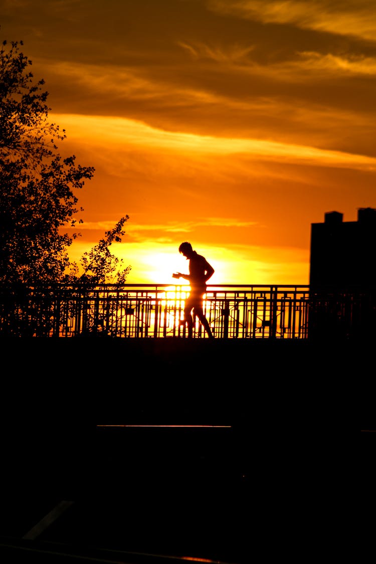 Silhouette Of A Man Jogging On A Bridge During Sunset