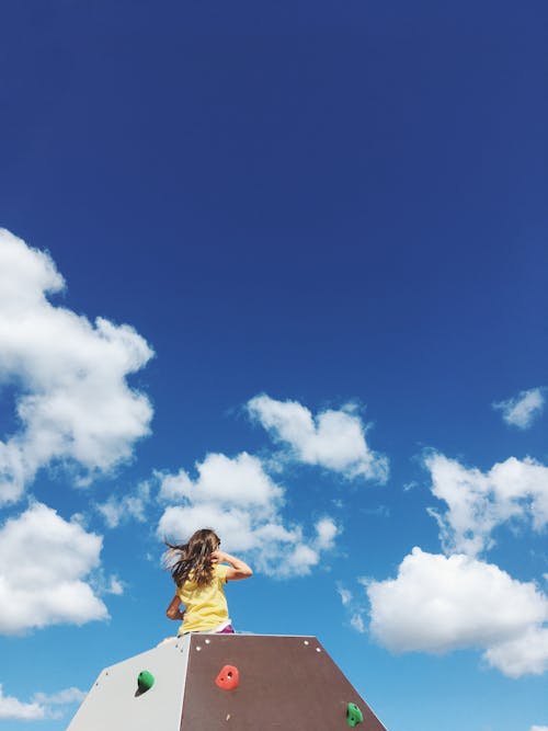 Free Girl sitting on Top of a Structure under Blue Cloudy Sky  Stock Photo
