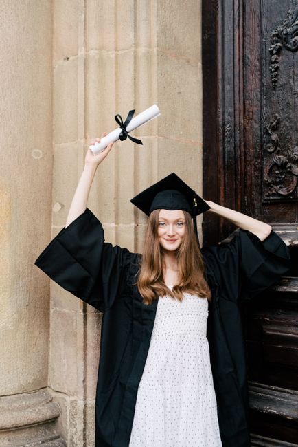 Young woman in graduation gown holding diploma outside with joy.