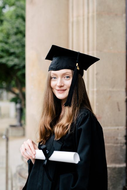 Young woman in graduation attire smiling with diploma outdoors, symbolizing achievement and success.