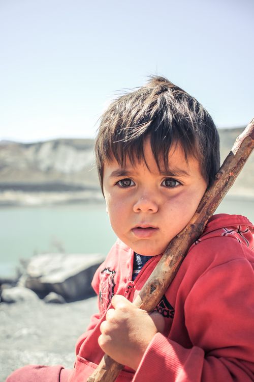 Free A young boy in a red jacket holding a stick, looking curious, outdoors near water. Stock Photo