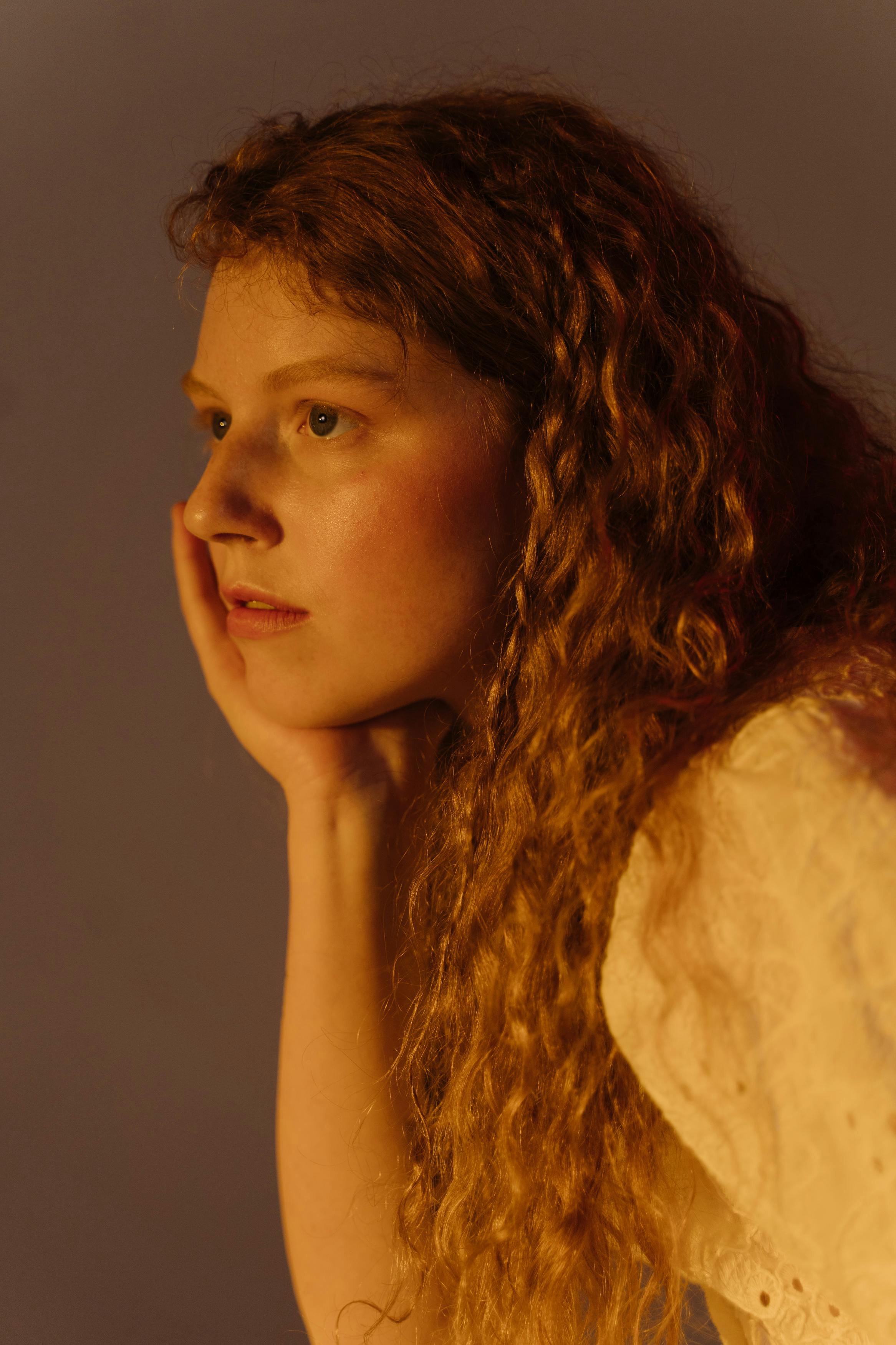 A thoughtful woman poses in soft lighting with her hand on her chin.