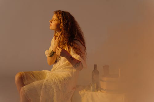 Woman in a White Dress Holding Hair While Sitting