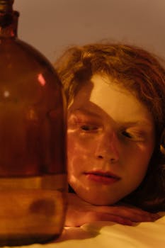 A woman with wavy hair gazes thoughtfully at a large brown glass jar, creating a play of light and shadow.