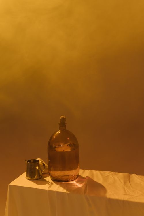 Free Aesthetic still life with a glass bottle and metal cup on a draped table. Stock Photo
