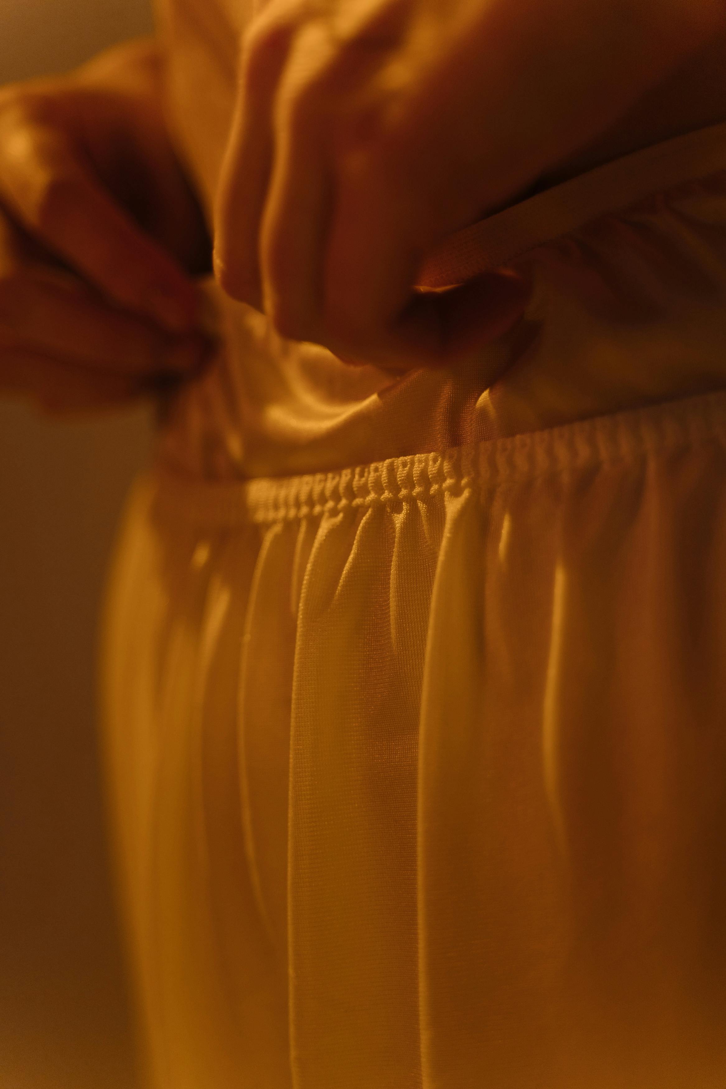 A detailed view of hands adjusting white fabric in warm lighting, highlighting texture and fashion details.