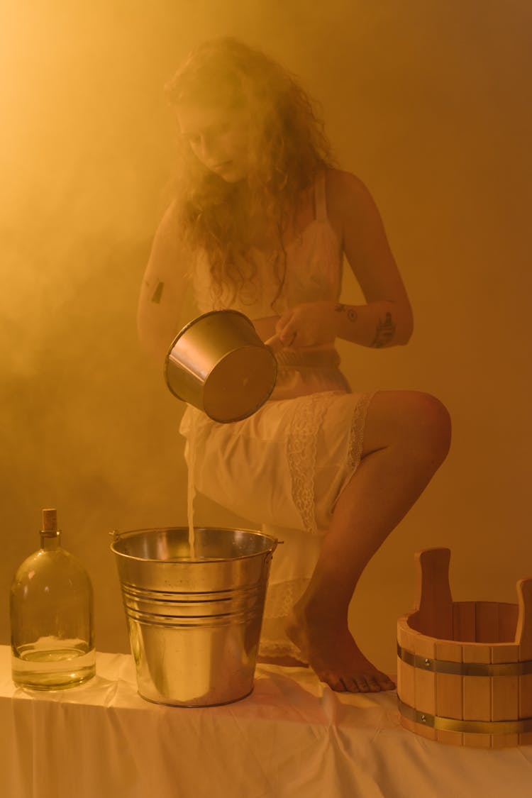 Woman Holding A Stainless Pot Pouring Water In A Bucket