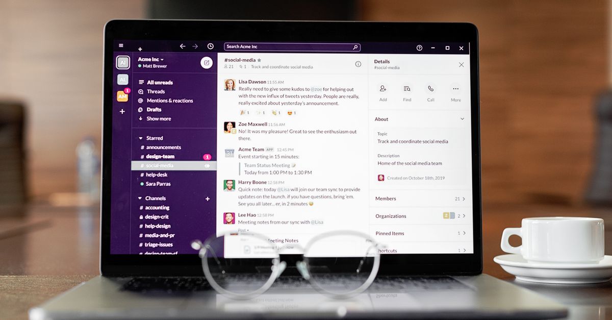 Laptop displaying a messaging app, with eyeglasses and coffee cup on a wooden table.
