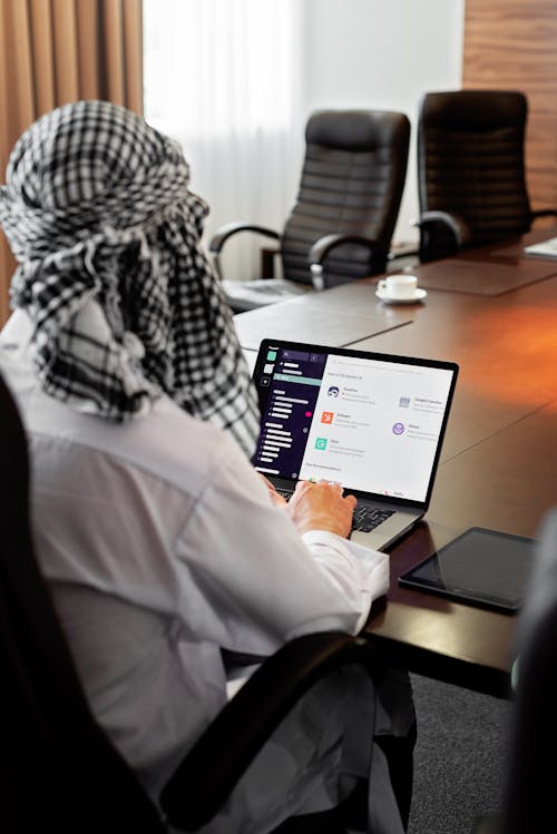 Person in White Dress Shirt Sitting on Chair in Front of Macbook Pro