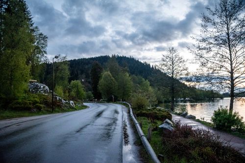 Free A peaceful road by a lake with mountain view during twilight, capturing nature's tranquility. Stock Photo