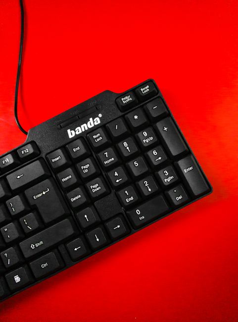 Fotomural Vista detallada de un teclado negro sobre una superficie roja vibrante, resaltando el diseño tecnológico moderno.