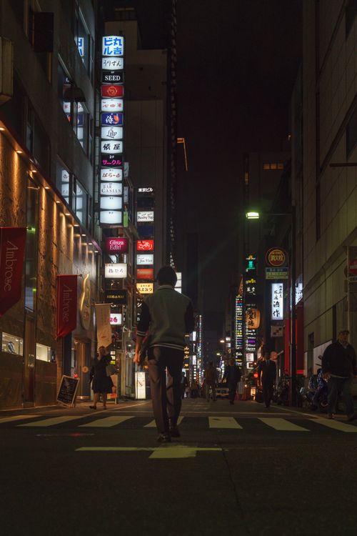 Free A person walks through a vibrant Tokyo street in Chuo City at night, surrounded by glowing signs and city life. Stock Photo