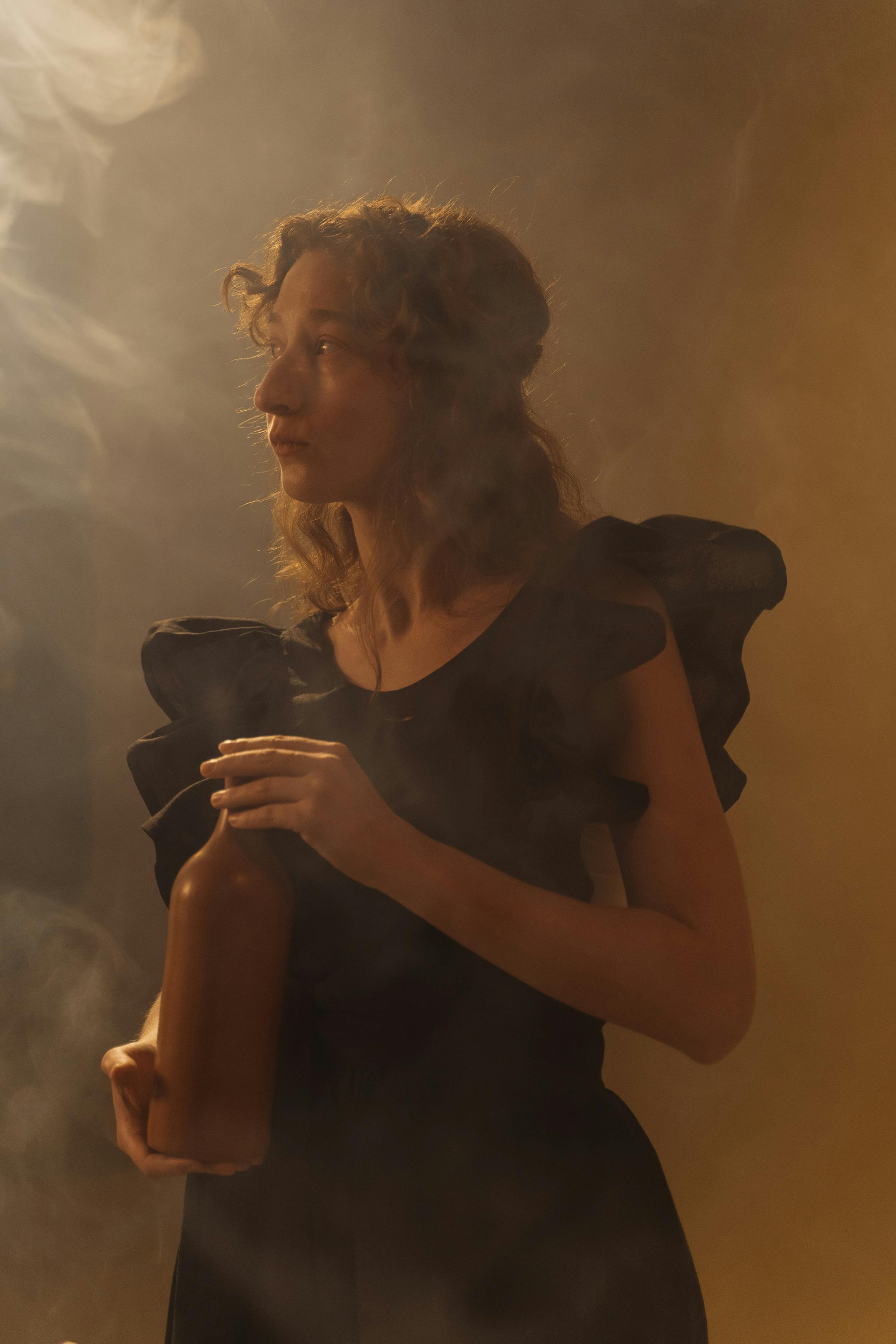 Artistic portrait of a woman holding a bottle amidst smoke, capturing a vintage mood.