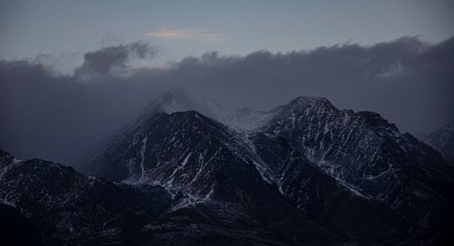 Breathtaking view of dark, snow-covered mountain peaks under a moody evening sky.