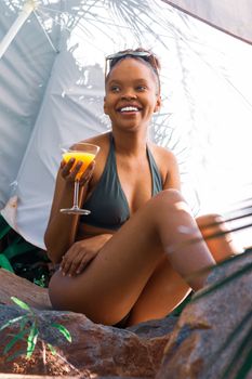 A joyful woman in a swimsuit holding a cocktail while relaxing by a poolside, enjoying a sunny day.